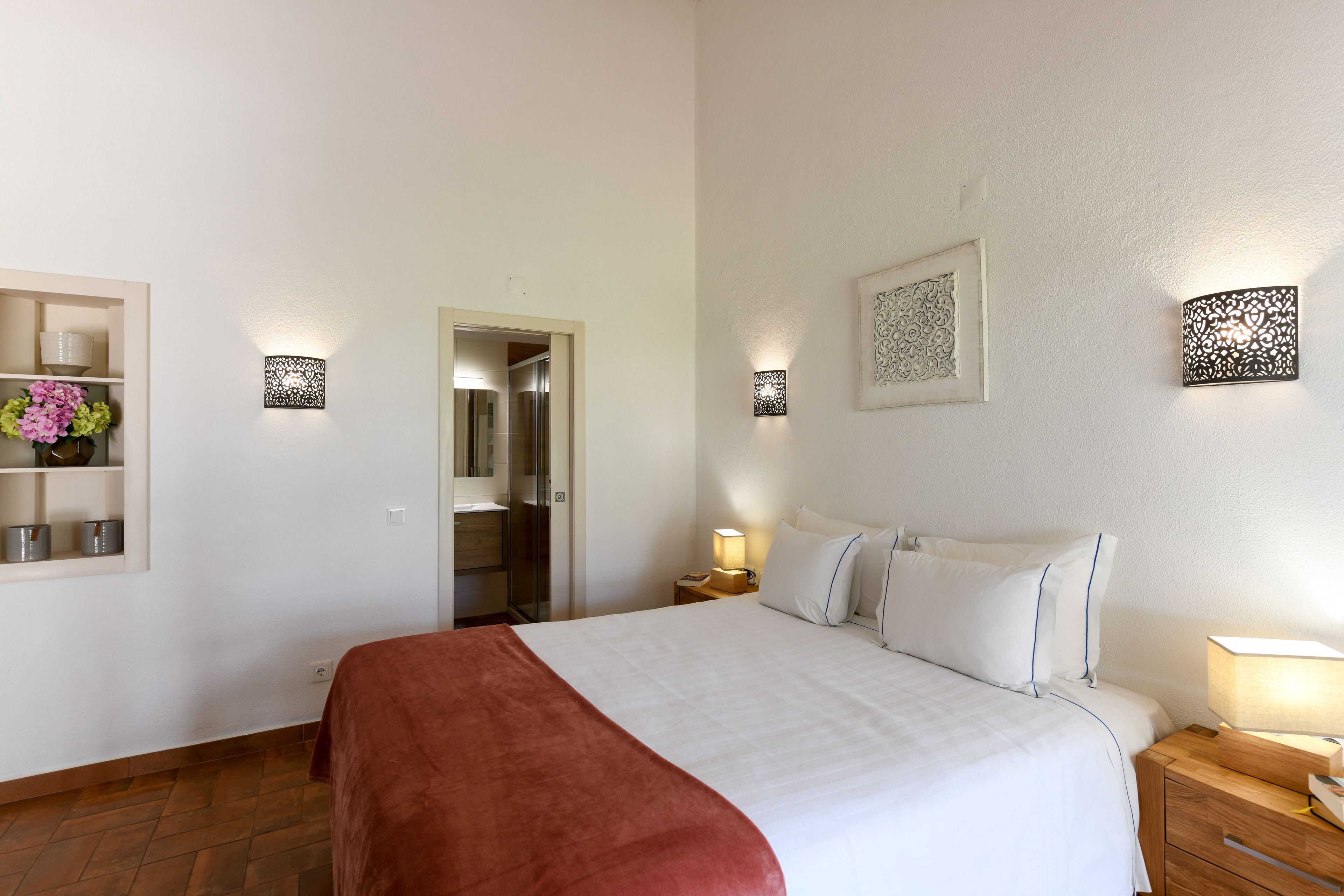 Een hotelkamer met een groot bed, een houten nachtkastje, een wandlamp en een plank met decoratieve objecten.