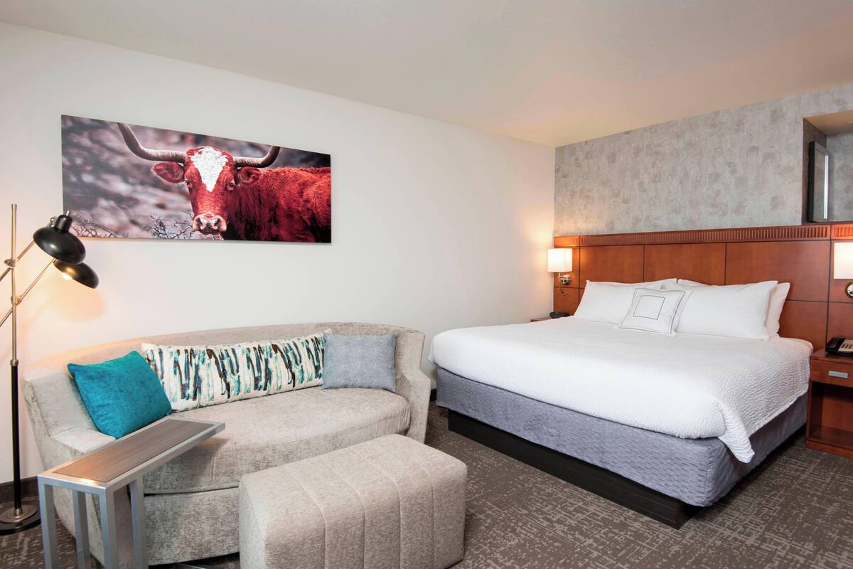Quarto de hotel com cama, sofá, uma mesinha e luminária fixada na parede.
