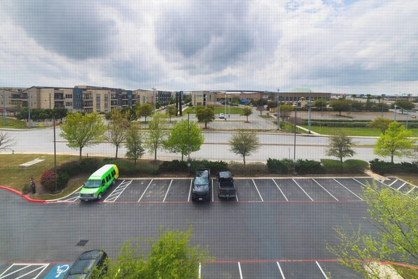 Vista aérea de un estacionamiento con varios coches y una furgoneta verde, rodeado de edificios y árboles.