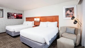Habitación de hotel con dos camas, cabecero de madera, un escritorio con lámpara y un cuadro en la pared.