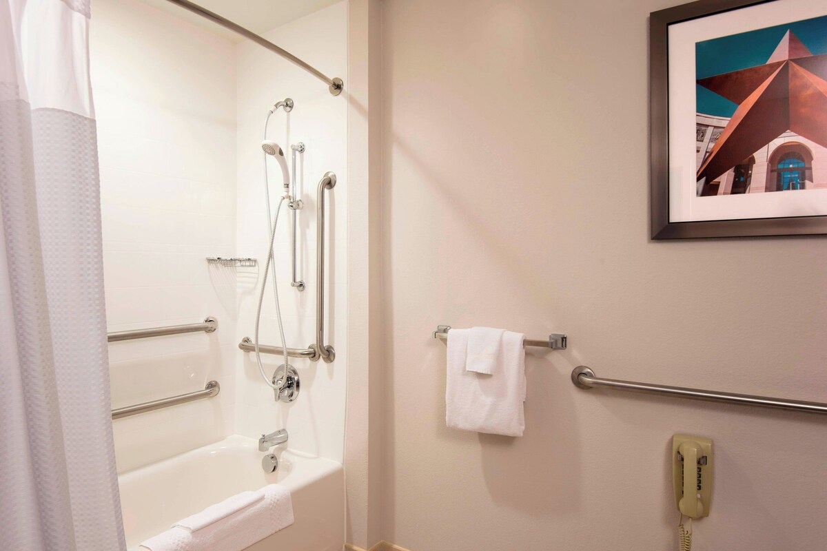 A bathroom with a bathtub, grab bars, a towel rack, a framed picture on the wall, and a telephone.