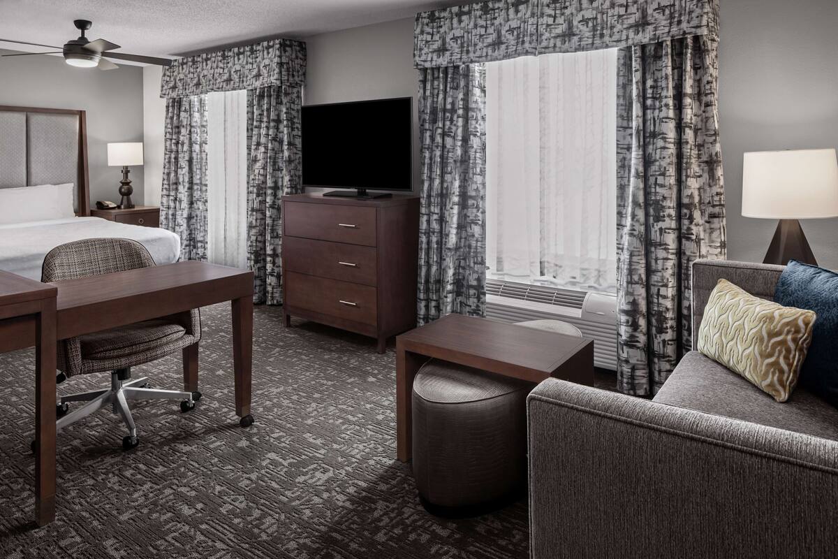 A hotel room with a bed, a desk, a television, a sofa, and a window with curtains.