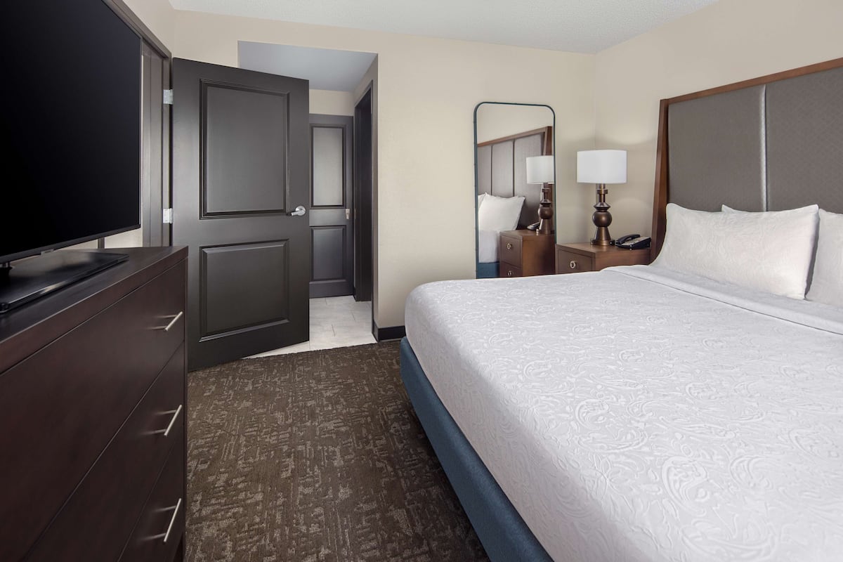 A hotel room with a large bed, a television on a dresser, a desk with a lamp, and a mirror.