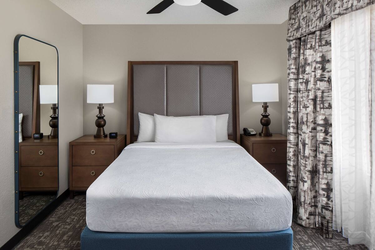 A hotel room with a large bed, two bedside tables with lamps, a mirror, and a ceiling fan.