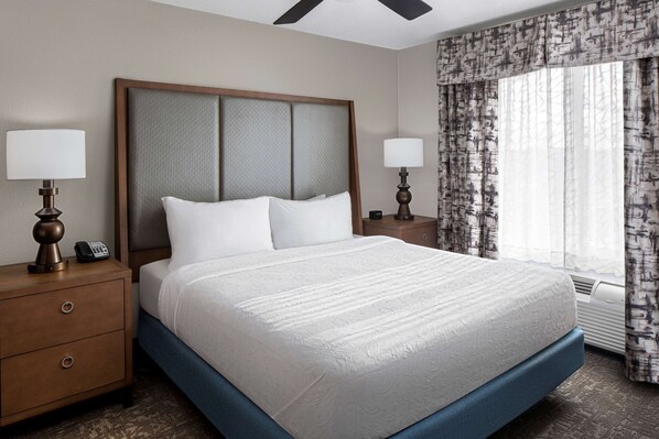 A neatly made bed with a wooden headboard, two bedside tables with lamps, and a patterned curtain.