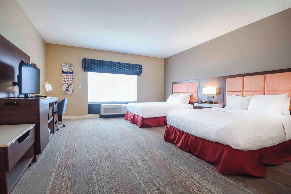 A hotel room with two beds, a desk, a television, and a window with a view.