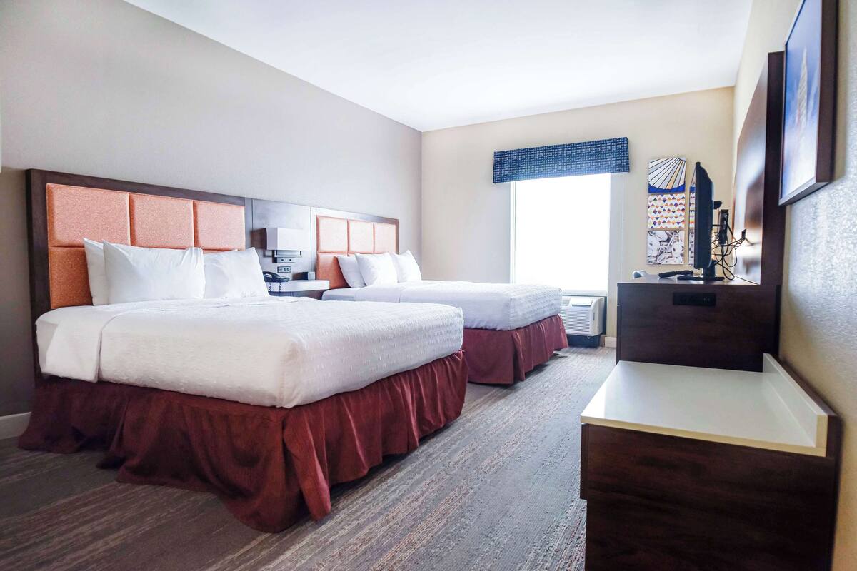 A hotel room with two beds, a desk, and a TV.