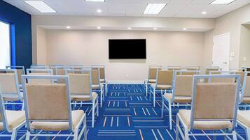 A conference room with rows of chairs, a large flat-screen TV on the wall, and a patterned carpet.