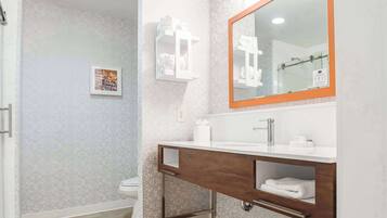 Un baño con lavamanos blanco, un espejo grande y un perchero para toallas.