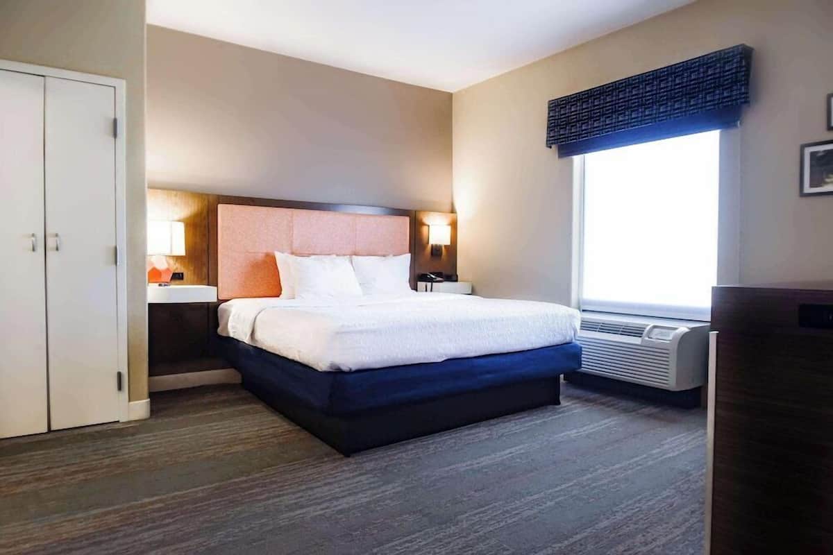 A hotel room with a bed, bedside table, lamp, and a window with a view.