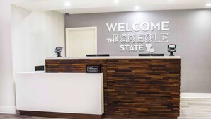 A reception desk with a "WELCOME TO THE CREOLE STATE" sign, a "Hilton Honors" badge, and a security camera. - Hampton Inn Baton Rouge - Denham Springs (Denham Springs)
