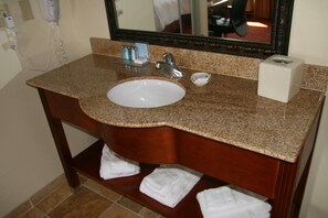 Un baño con encimera de granito, un lavabo blanco, un espejo y un perchero para toallas.