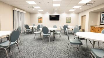 A conference room with multiple tables and chairs, a flat-screen TV mounted on the wall, and a carpeted floor.