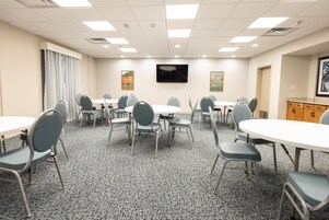 A conference room with multiple tables and chairs, a flat-screen TV mounted on the wall, and a carpeted floor.
