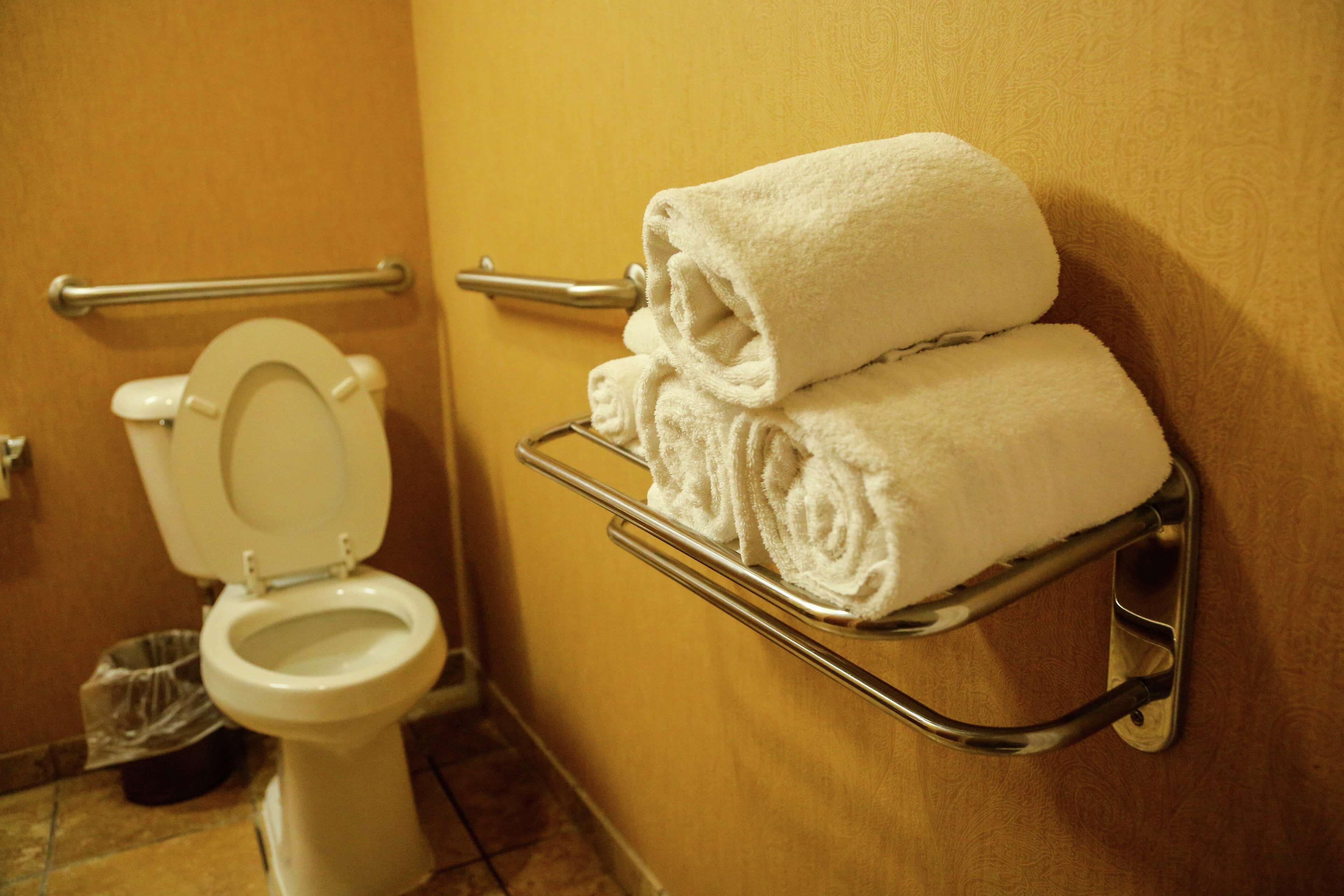 A bathroom with a white toilet, a towel rack with folded towels, and a handrail.