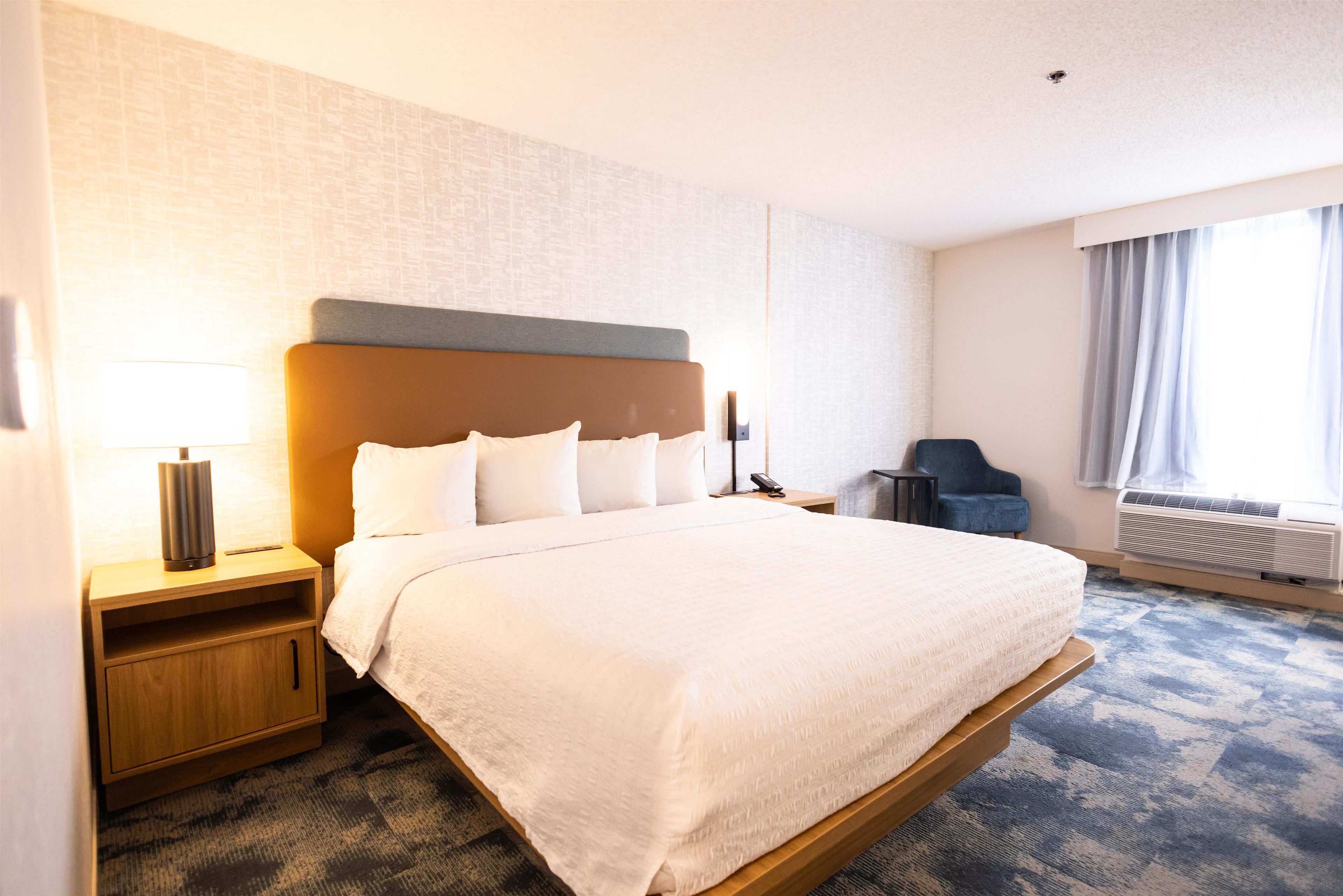 Une chambre d’hôtel avec un grand lit, une table de chevet, une chaise, un bureau et une fenêtre avec des rideaux.