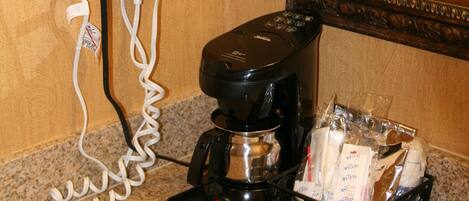 A hotel bathroom with a hairdryer, coffee maker, and toiletries on the counter.