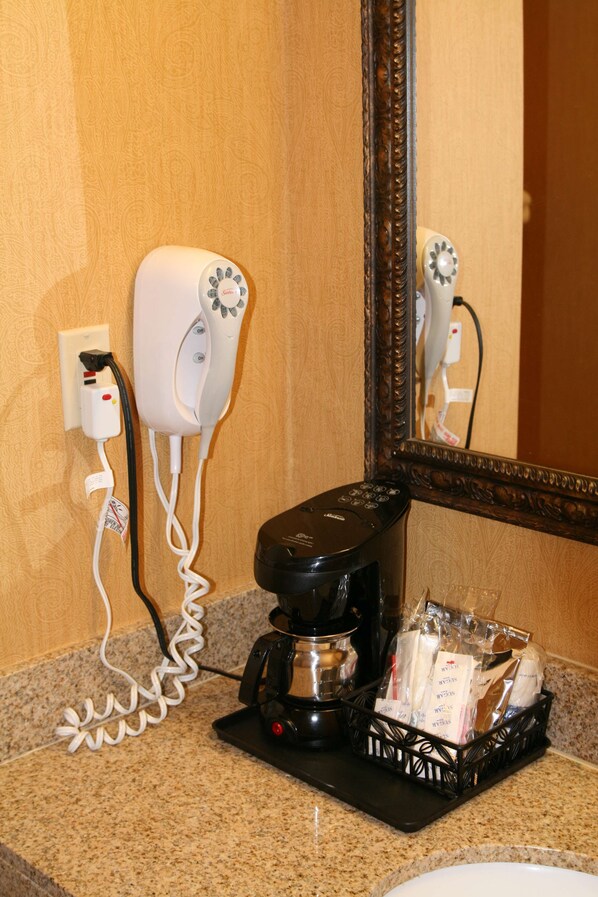 Un baño de hotel con secador de pelo, cafetera y artículos de aseo sobre el mostrador.