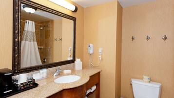 A bathroom with a large mirror, sink, and toilet. There is a hairdryer and a trash can visible.