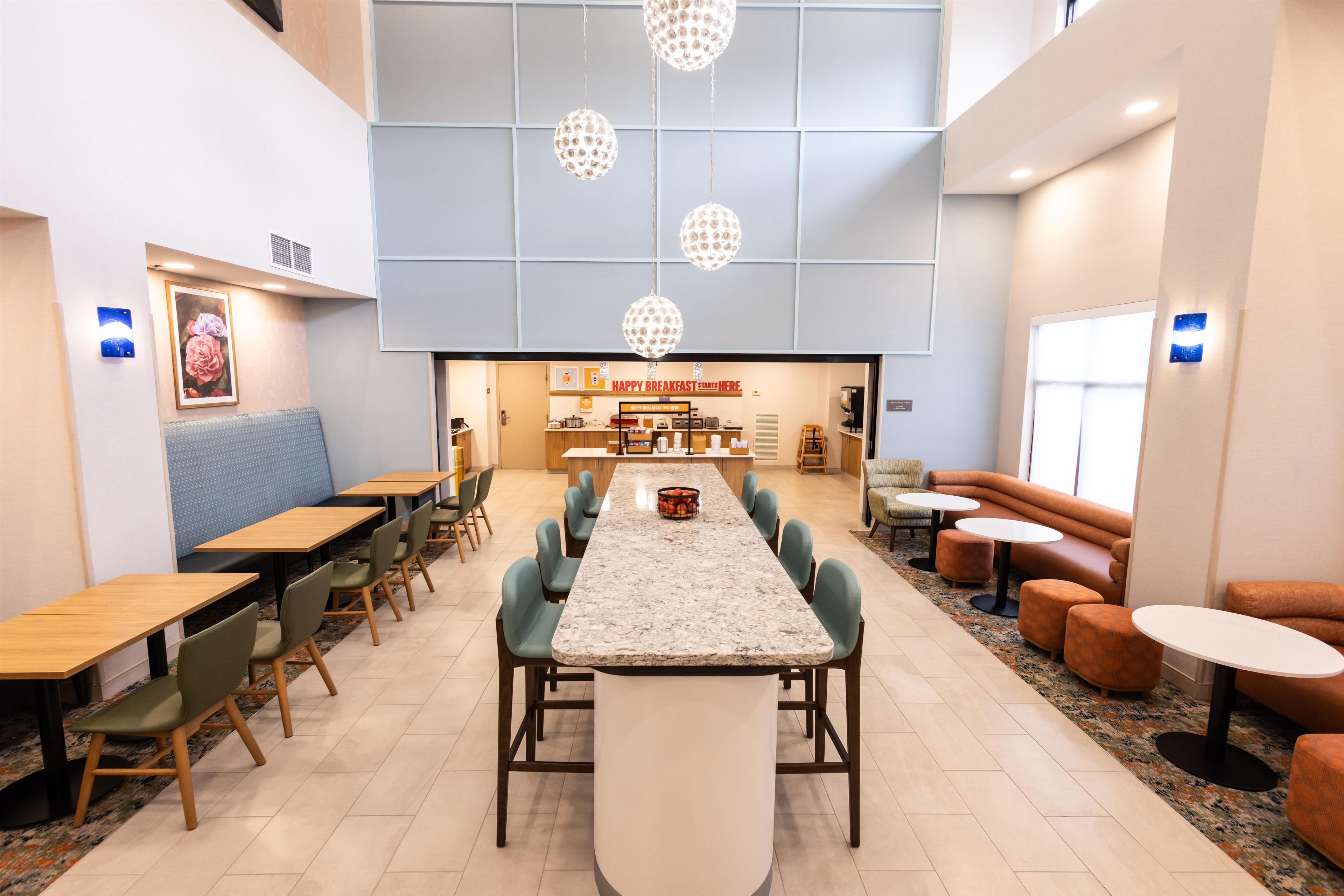 A modern dining area with a long communal table, multiple seating options, and a visible breakfast bar.