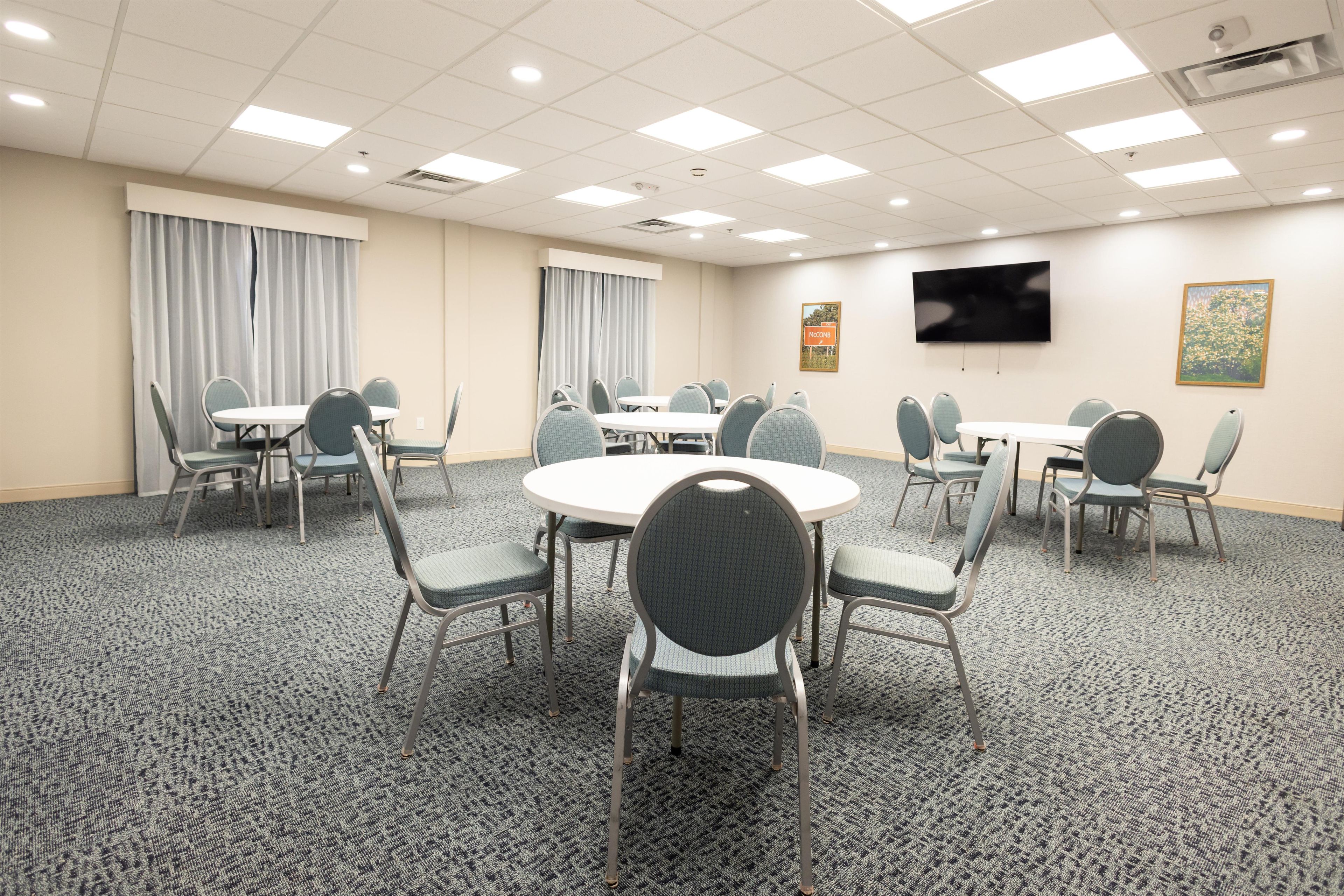 A conference room with round tables, chairs, a flat-screen TV, and curtains.