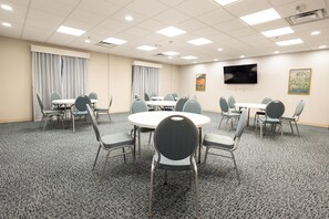 A conference room with round tables, chairs, a flat-screen TV, and curtains. - Hampton Inn & Suites McComb (McComb)