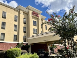 Et fleretagers hotel med en beige facade, en klar himmel og et skilt med teksten 'Hampton Inn & Suites'.