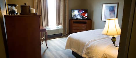 Habitación de hotel con cama, televisión, escritorio, lámpara y ventana con cortinas.