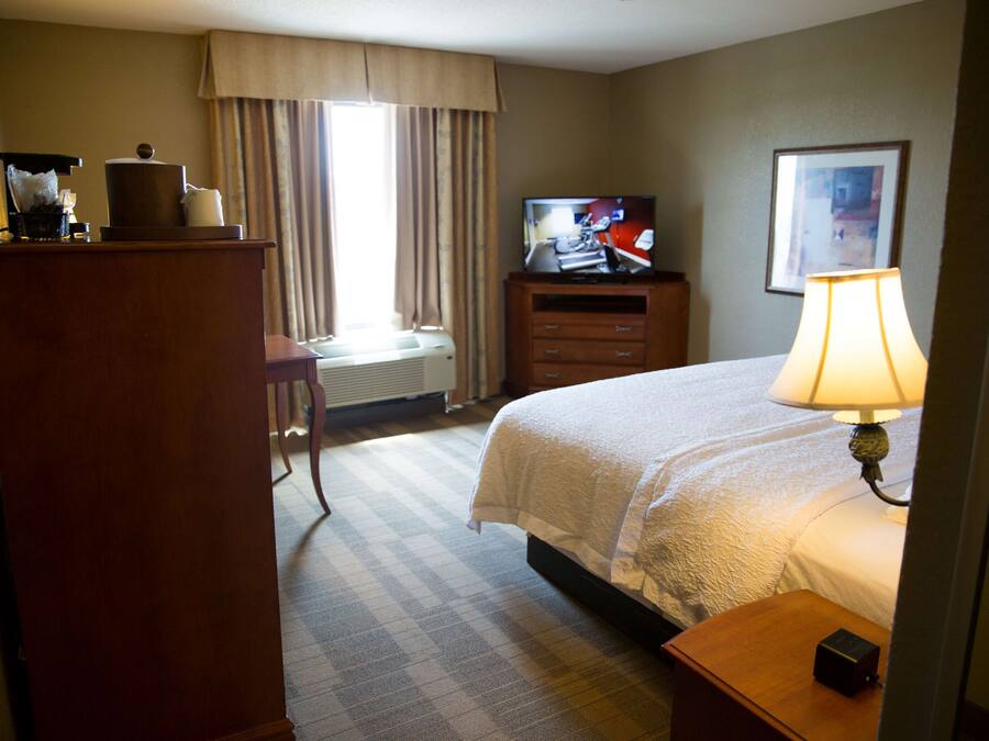 A hotel room with a bed, a television, a desk, a lamp, and a window with curtains.