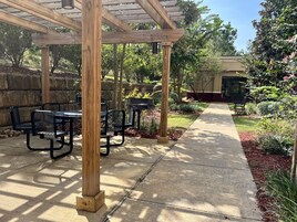 Un espace extérieur aménagé en terrasse, doté de structures en bois formant une pergola, de tables et de chaises en métal.