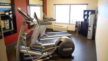 A gym with treadmills and a stationary bike, a window with blinds, and a wall clock.