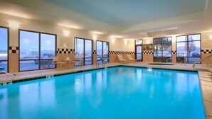 An indoor swimming pool with clear glass walls, lounge chairs, and a lifeguard sign.