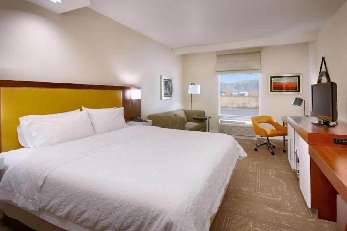 A hotel room with a large bed, a desk, a chair, a TV, and a window with a view.