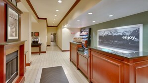 A hotel lobby with a reception desk, a fireplace, framed pictures on the wall, and a large poster with the word "enjoy."