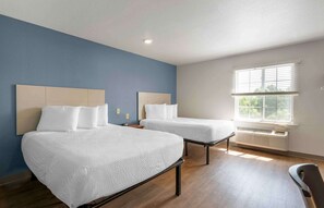 A hotel room with two beds, a window with blinds, a heater, and a chair. - Extended Stay America Select Suites - Lakeland (Lakeland)