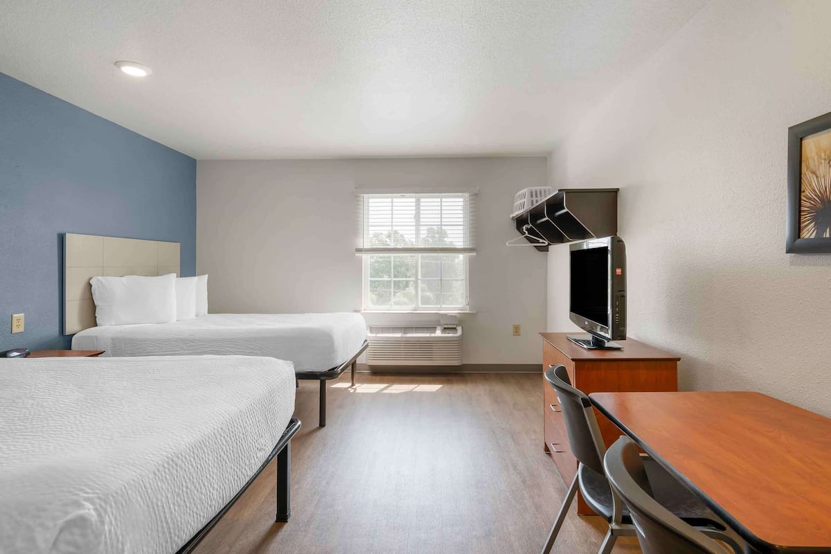A hotel room with two beds, a desk, a television, and a window with blinds.