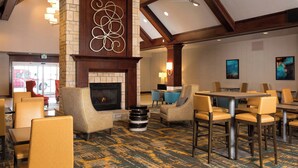 A hotel lobby with a fireplace, seating areas, and a dining section. - Residence Inn by Marriott Kansas City Airport (Kansas City)