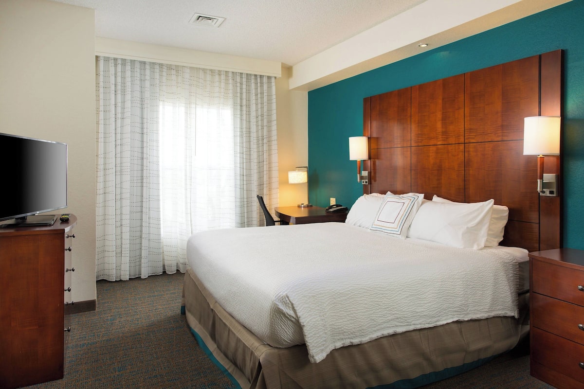 A hotel room with a large bed, a desk, a television, and a window with curtains.