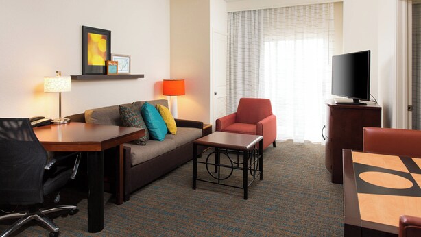 A hotel room with a sofa, armchair, coffee table, TV, and a desk with a lamp. - Residence Inn by Marriott Kansas City Airport (Kansas City)
