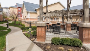 A covered outdoor patio with brick pillars and tables, adjacent to a building with a sloped roof. - Residence Inn by Marriott Kansas City Airport (Kansas City)
