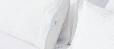Una cama con ropa de cama y almohadas blancas, una de ellas con el logo 'Pure'.