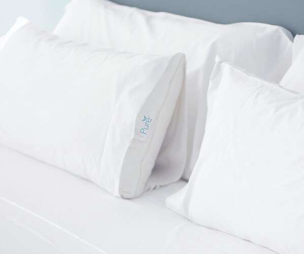 Una cama con ropa de cama y almohadas blancas, una de ellas con el logo 'Pure'.