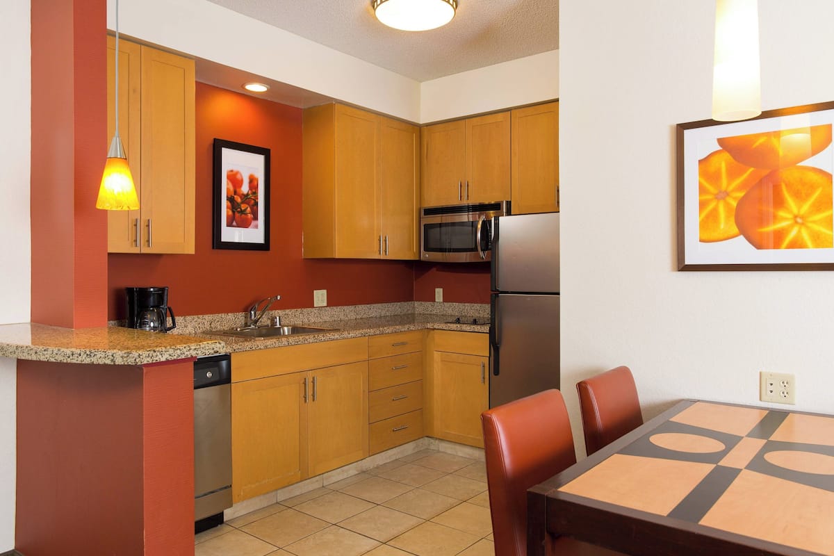 A compact kitchen with wooden cabinets, a microwave, a refrigerator, and a dining table with chairs.