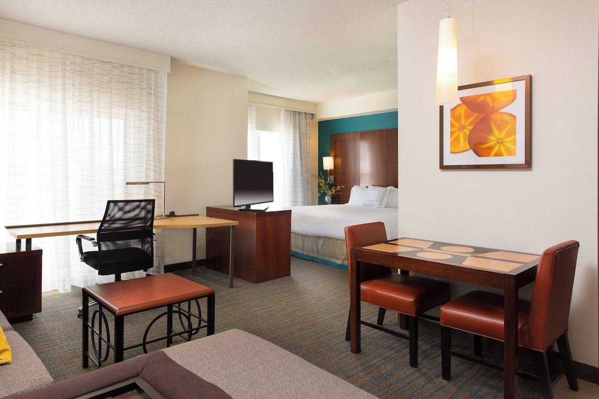 A hotel room with a bed, desk, TV, and seating area.