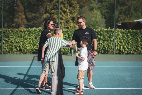 Una cancha de tenis con una red, rodeada por una cerca de malla y follaje.