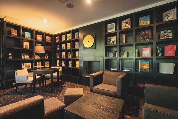 Um espaço aconchegante para leitura com lareira, estantes de livros, assentos confortáveis e uma mesa.