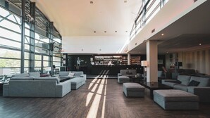Un vestíbulo amplio con zona de bar, ventanas grandes y mobiliario moderno.