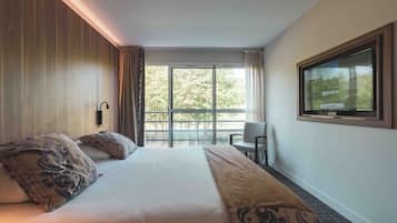 A hotel room with a large bed, a television, and a balcony with a view of trees.