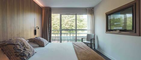 Una habitación de hotel con una cama grande, televisión y balcón con vistas a árboles.