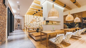 A modern interior with a long hallway leading to a seating area with tables and chairs, wooden beams on the ceiling, and a brick wall on one side. - Atour Hotel International Trade Jinsong Beijing (Beijing)